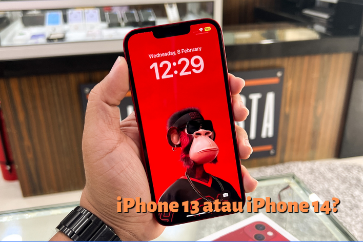 Gambar iPhone 13 dengan wallpaper berwarna merah, dengan caption: iPhone 13 atau iPhone 14