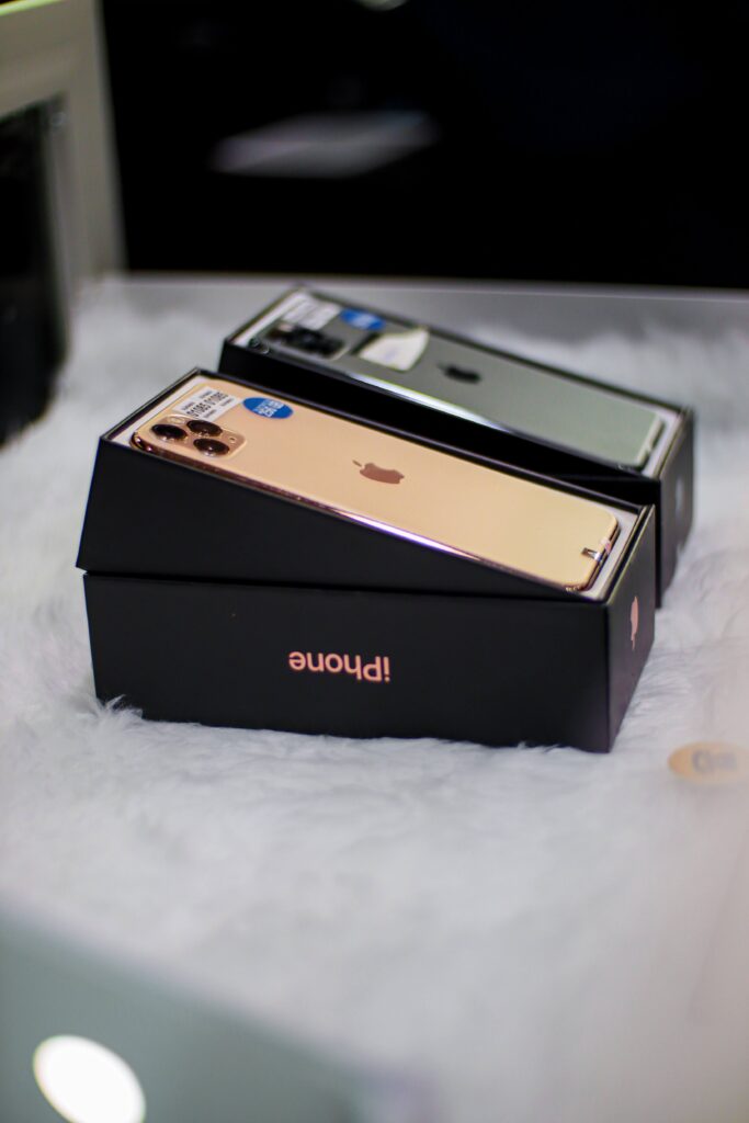 Gambar dua buah iPhone 11 Pro Max (berwarna gold dan hijau) yang berada dalam sebuah display showcase.